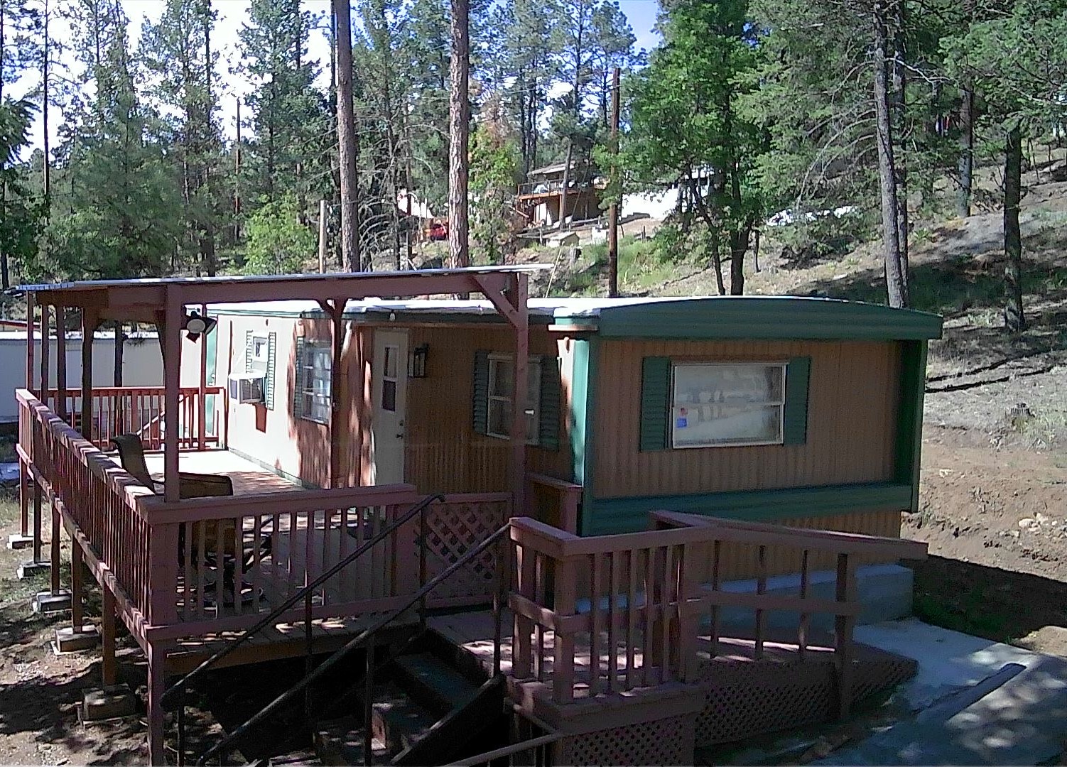 Front exterior of the cabin featuring a wooden deck with protective railing, set against a backdrop of dense forest and sloping hillside, conveying a secluded mountain location